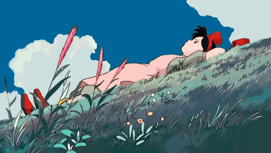 Kiki resting in a windswept meadow beneath a blue summer sky.